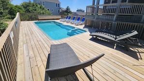 A wooden deck with a swimming pool, lounge chairs, and a wooden fence.