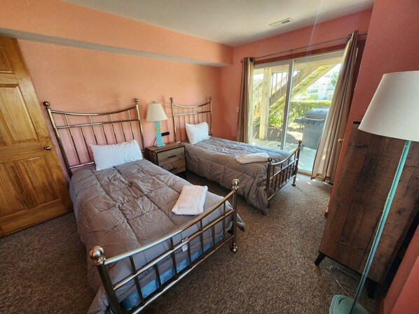 A room with two beds, a wooden wardrobe, a nightstand, and a window with curtains.