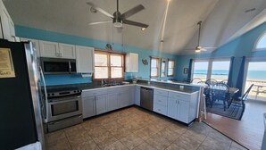 Una cocina con una isla grande, ventilador de techo y vista al océano.