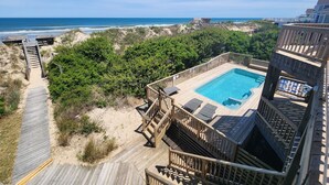 Una terraza de madera que da a una piscina con vistas a la playa y al océano.