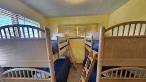 A room with bunk beds, a window with blinds, and a carpeted floor.