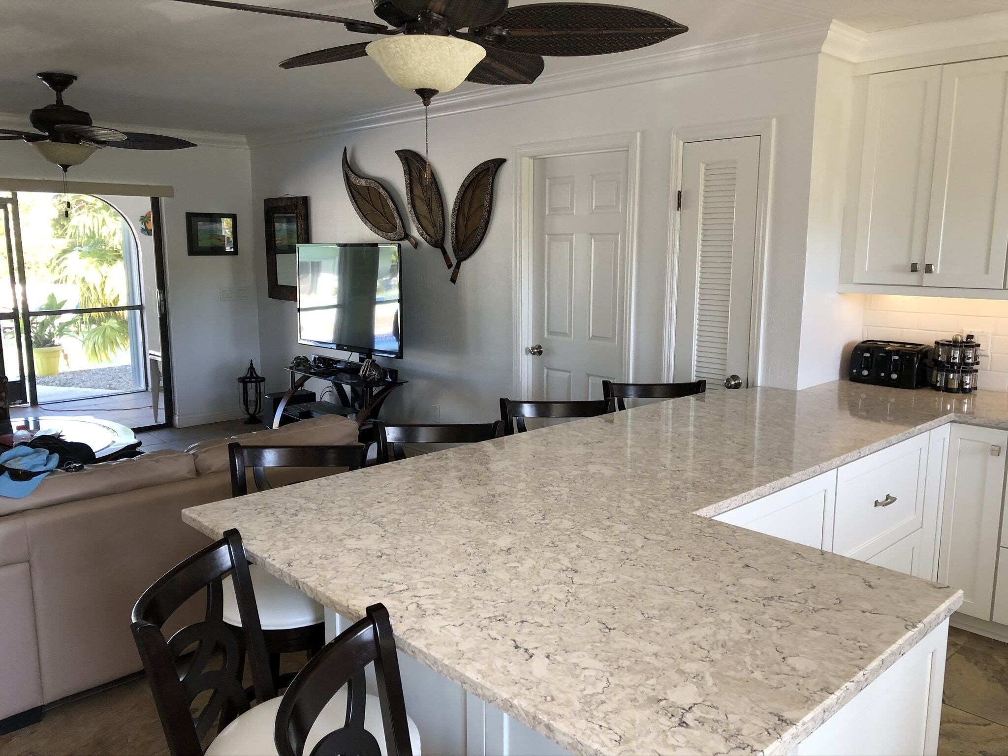 A kitchen with a large island, white cabinets, a ceiling fan, and a television.