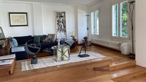 Un salon spacieux doté d’un plancher en bois, d’un canapé de couleur foncée, d’une table basse en verre et d’une grande fenêtre laissant entrer la lumière naturelle.