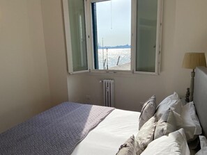 Een slaapkamer met een bed, een raam met gordijnen, een radiator en een lamp.