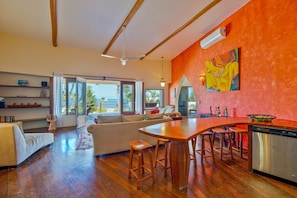 A spacious living area with a large window, a kitchen with a bar, and a dining area.