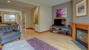 Ein modernes Wohnzimmer mit grauem Sofa, einem Flachbildfernseher, einem Kamin und einer Treppe, die in einen anderen Raum führt.