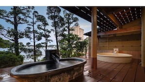 Un jacuzzi de piedra y una terraza de madera con vistas a árboles y un edificio al fondo.