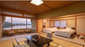 Una habitación japonesa tradicional con suelo de tatami, una mesa baja con cojines, dos camas y vista a un cuerpo de agua.