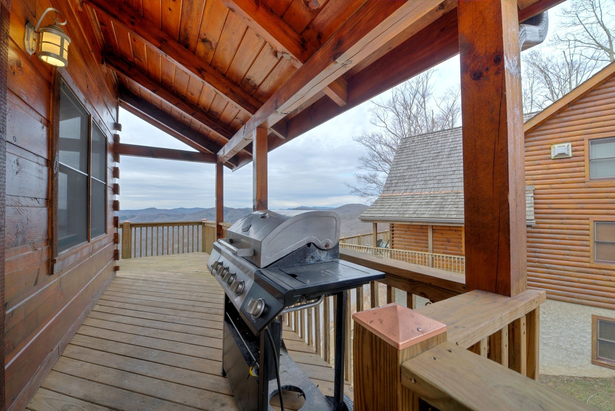 A wooden deck with a grill and a wooden table, overlooking a mountainous landscape.