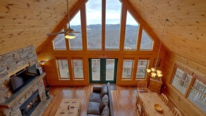 Um amplo quarto no estilo loft com um grande teto de madeira, lareira de pedra, sofá de couro e mesa de jantar.