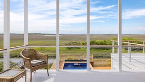 Un balcon avec un fauteuil en osier, un jacuzzi et une vue sur un paysage verdoyant.