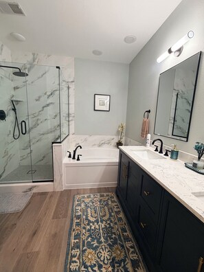 A bathroom with a glass shower enclosure, a bathtub, a large mirror, and a sink with dark cabinets. - Relax In Luxury On Table Rock Lake, Close To Branson (Hollister)