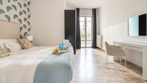 Ein Hotelzimmer mit Bett, Schreibtisch mit Stuhl, Fernseher und einem Balkon mit Vorhängen.