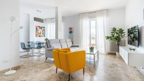 Ein modernes Wohnzimmer mit einer Couch, einem gelben Sessel, einem Essbereich und einem Fernseher.