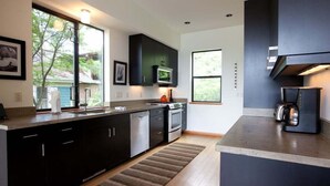 Una cocina moderna con armarios oscuros, electrodomésticos de acero inoxidable y ventanas amplias con vistas a zonas verdes.