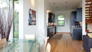 Una cocina moderna con armarios oscuros, una isla central y una zona de comedor con mesa y sillas de vidrio.