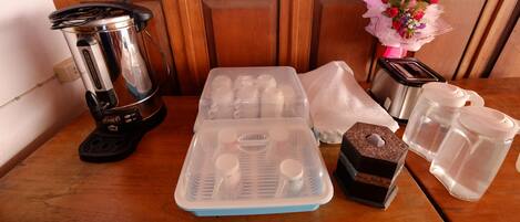 Una encimera de cocina con una cafetera, tazas medidoras, un pastel, una jarra de agua y un arreglo floral decorativo.