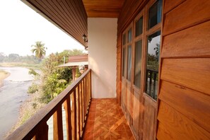 Un balcón de madera con piso de baldosas, con vista a un río y vegetación.