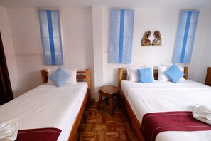 Habitación de hotel con dos camas individuales, cabeceros de madera, ropa de cama blanca, cortinas azules y un taburete de madera.