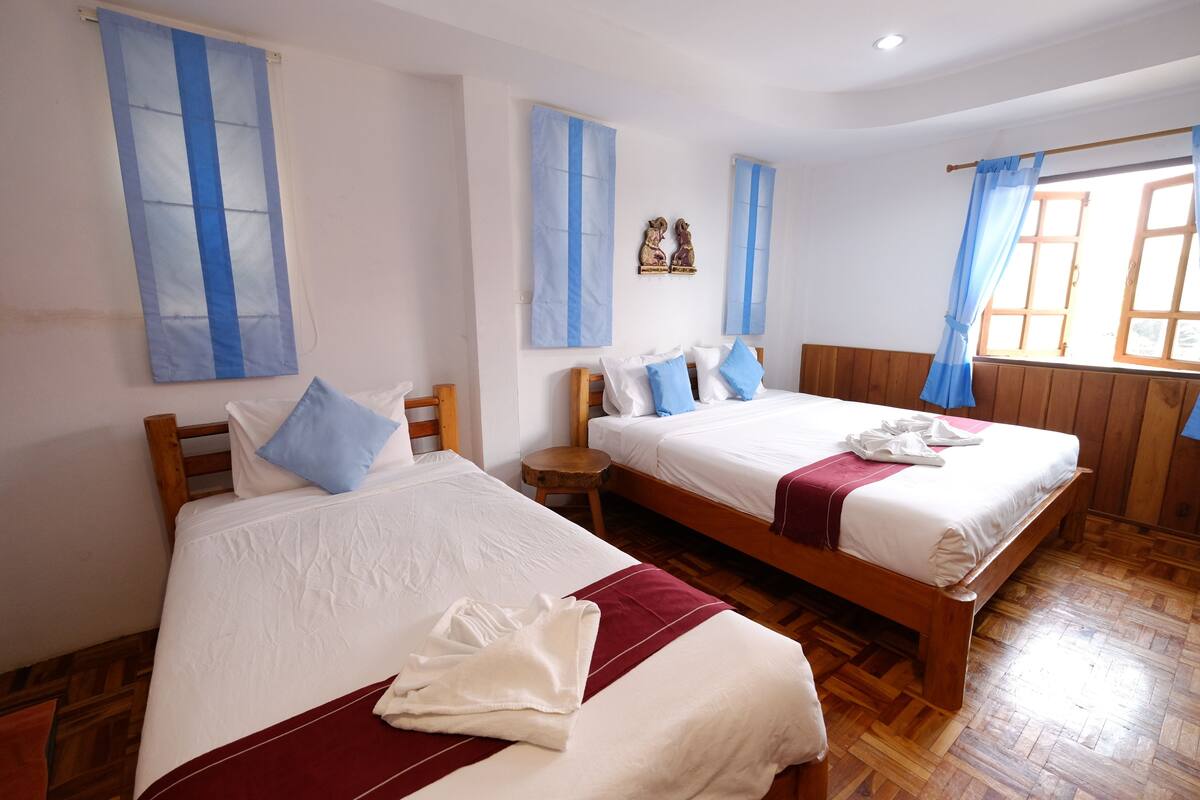 Quarto de hotel com duas camas, cabeceiras de madeira e cortinas azuis.