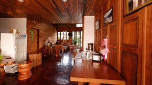 A wooden interior with a long dining table, wooden stools, and a refrigerator.
