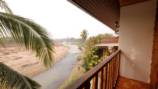 A balcony with a view of a river, palm trees, and a building with a tiled floor.