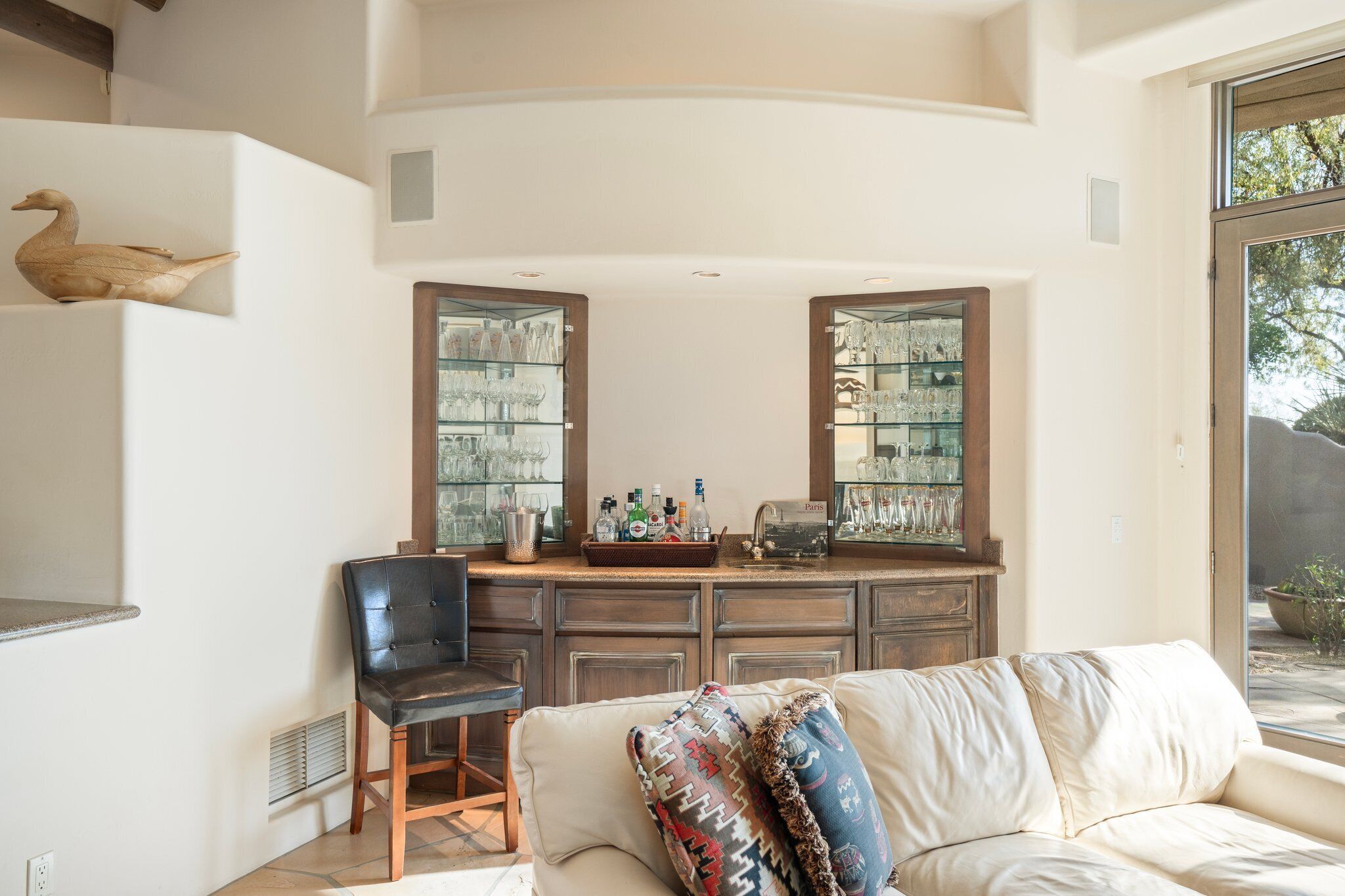 A living room with a white sofa, a black chair, and a wooden cabinet with glass doors displaying glassware.