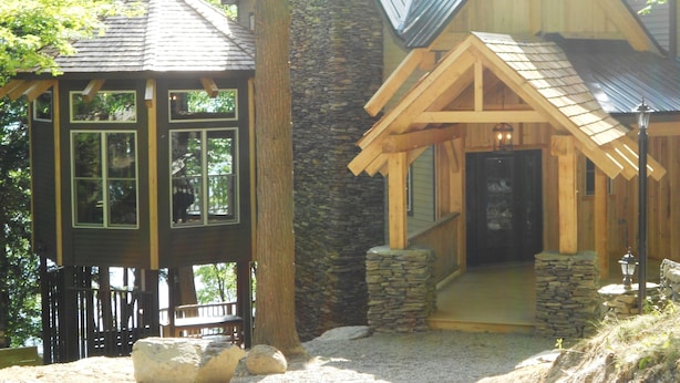 Une cabane en bois avec une cheminée en pierre, une terrasse en bois et un escalier en pierre menant à l’entrée.