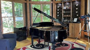 Un piano à queue dans une pièce dotée de grandes fenêtres, un bar en bois avec des bouteilles de vin et un télescope.