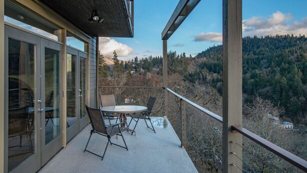 A balcony with a table and chairs, overlooking a forested hillside. - Hazel House - Gorgeous, Views, Perfect Hood River Getaway! (Hood River)