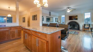 A spacious living area with a fireplace, a ceiling fan, and a large island with a granite countertop. - Hazel House - Gorgeous, Views, Perfect Hood River Getaway! (Hood River)