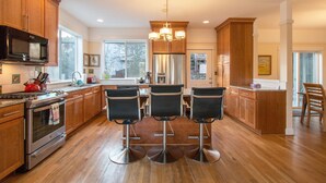A modern kitchen with wooden cabinets, stainless steel appliances, and three bar stools. - Hazel House - Gorgeous, Views, Perfect Hood River Getaway! (Hood River)