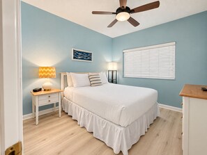 Een slaapkamer met een bed, nachtkastjes, een plafondventilator, een raam met zonwering, en een kunstwerk aan de muur.