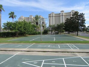 Un terrain de basket avec un panier, entouré d’arbres et avec des bâtiments en arrière-plan.