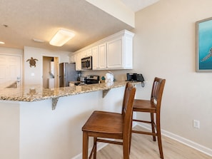 A kitchen with white cabinets, a granite countertop, and two wooden bar stools.