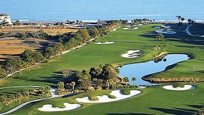 Un parcours de golf avec des obstacles d’eau, des bunkers de sable et un club-house en arrière-plan.