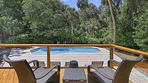 Une terrasse dotée de chaises et d’une table en osier, offrant une vue sur une piscine entourée d’une végétation luxuriante.