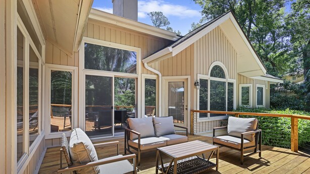 Une terrasse en bois avec des meubles d’extérieur, notamment un canapé et des fauteuils, et de grandes fenêtres.
