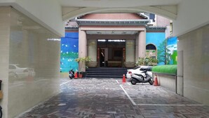 Entrada de un hotel con suelo de baldosas, una escalera que lleva a la entrada y algunas scooters estacionadas.