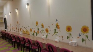 Un salón de conferencias con una larga mesa, filas de sillas y una pared decorada con girasoles y mariposas.