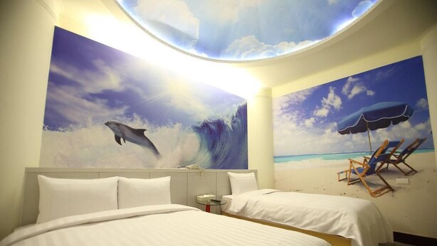 Habitación de hotel con dos camas, un mural en el techo que representa a un delfín y una playa, y vista al océano a través de un tragaluz.