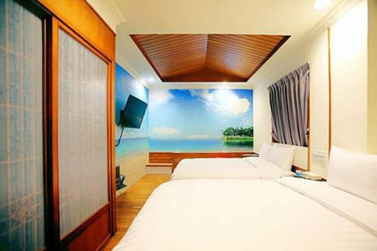 A hotel room with a bed, a TV, and a view of a beach through a window.