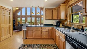 A kitchen with wooden cabinets, a stainless steel sink, and a large window overlooking a scenic view. - Skylands by Carolina Mornings | Hot Tub + Biltmore Pass 8 mins to Hatley Pointe (Mars Hill)