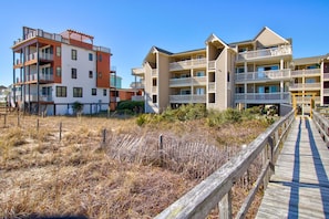 Een hotel aan het strand met meerdere balkons, een houten looppad en een zandstrand.
