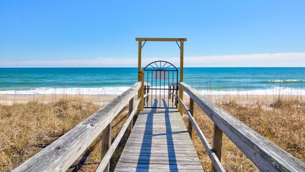 A wooden boardwalk leading to a beach with a metal gate structure.