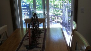 A dining area with a wooden table, chairs, and a view through a glass door to an outdoor space with greenery.