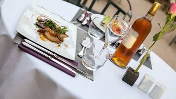 A dining table set with a plate of food, cutlery, glasses, and a bottle of wine.