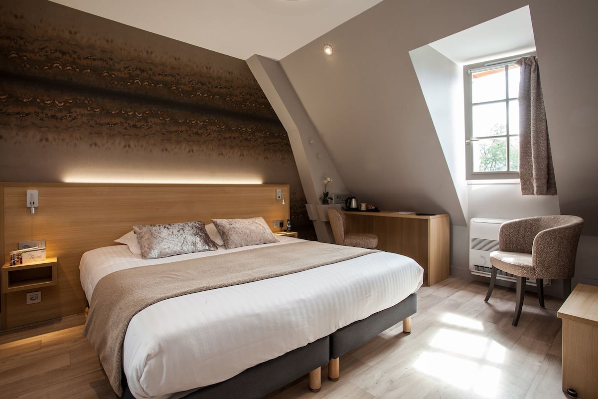 Un dormitorio con una cama grande, un escritorio, una silla y un ventanal con cortinas.