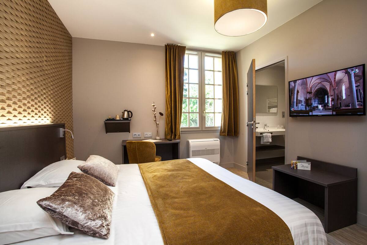 Habitación de hotel moderna con una cama grande, un televisor, un escritorio y un baño visible a través de una puerta abierta.
