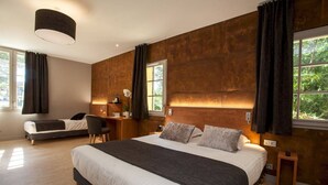 Une chambre moderne avec un grand lit, un bureau et une chaise. Elle est dotée de deux fenêtres avec des rideaux, et un mur en bois apporte une touche d’originalité à la pièce.